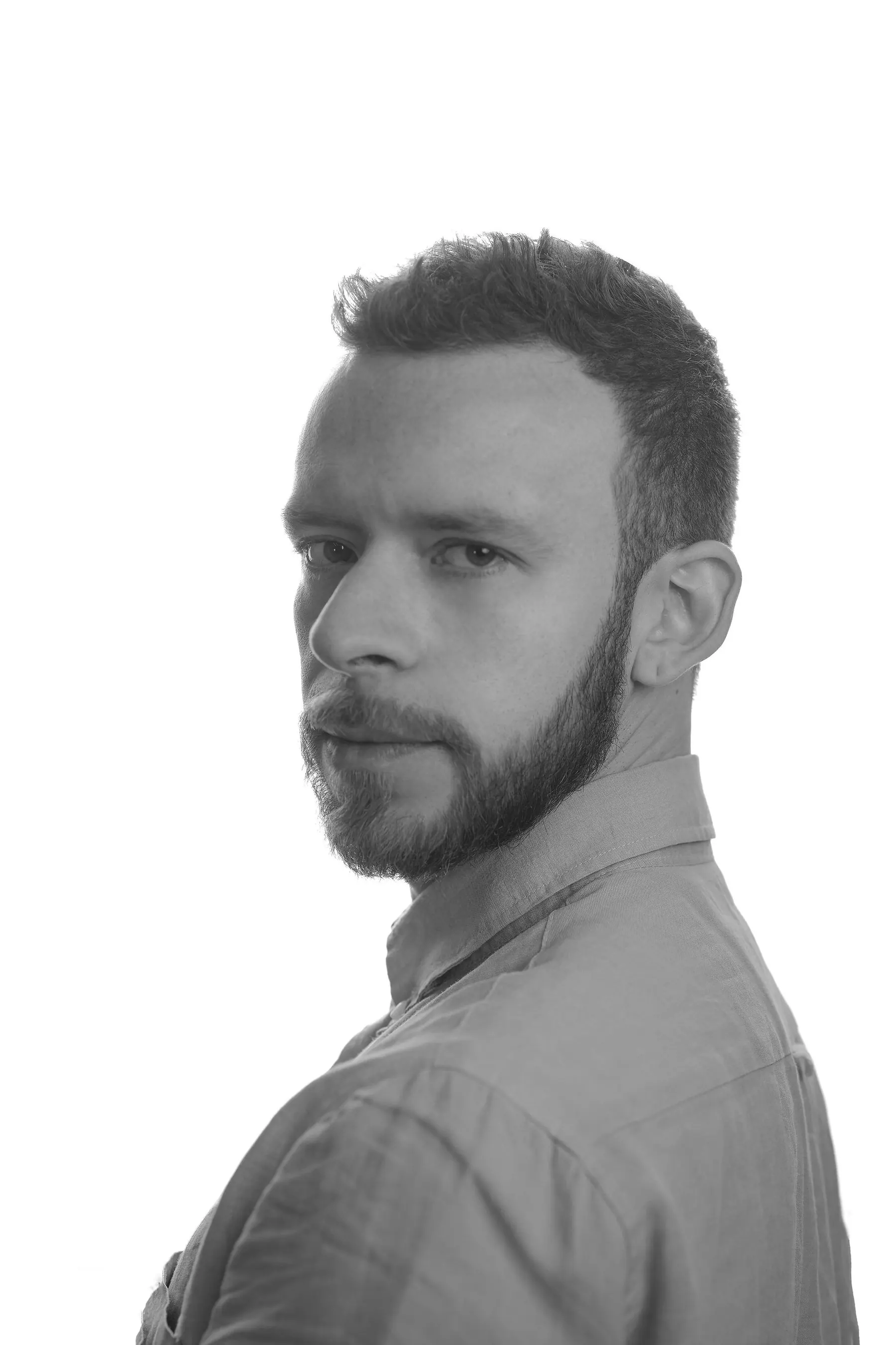 Retrato en blanco y negro de tres cuartos sobre fondo claro, camisa de cuello abierto y mirada a cámara.